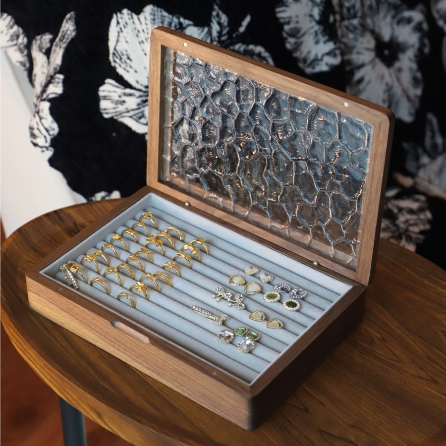Walnut ring and earring box with jewelry arranged in rows beneath an open glass lid