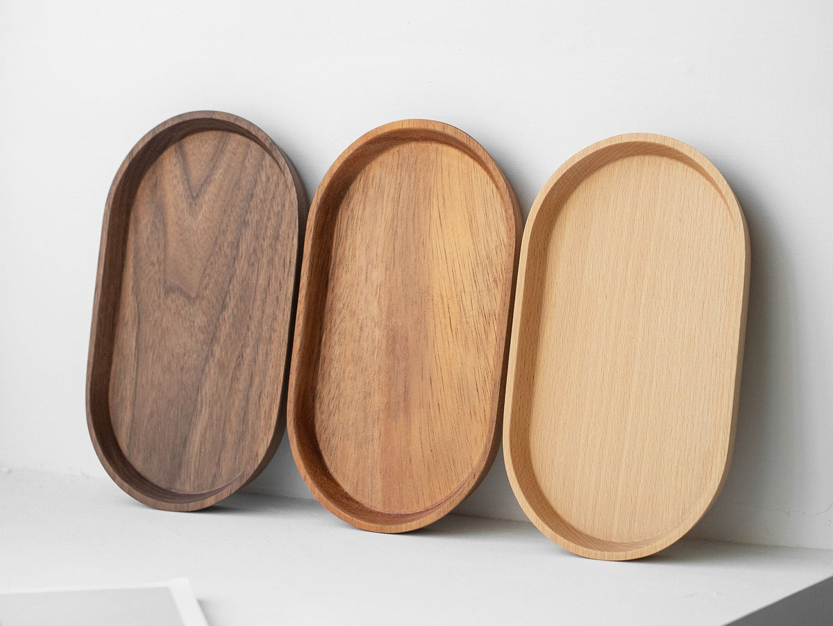 Three 8-inch oval coffee trays in walnut, acacia and beech leaning on a wall